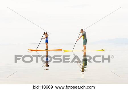 Couple riding paddle boards View Large Photo Image Stock Photo - Couple riding paddle boards. Fotosearch