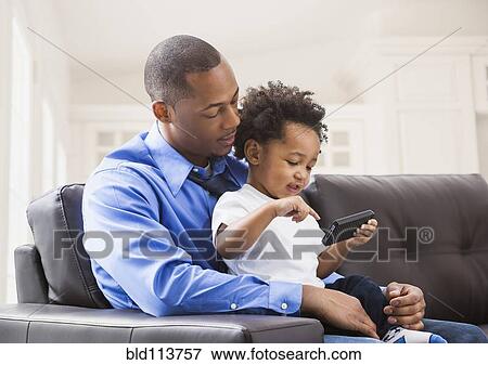 Stock Photo - Father and son playing with cell phone on sofa. Fotosearch