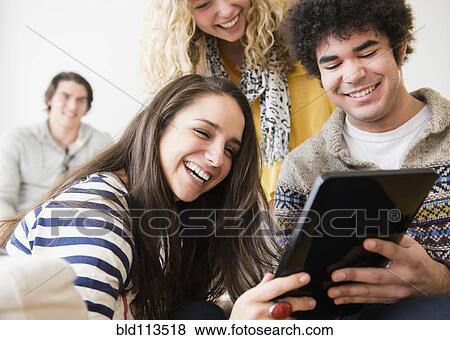 Stock Photo - Friends using tablet computer in living room. Fotosearch