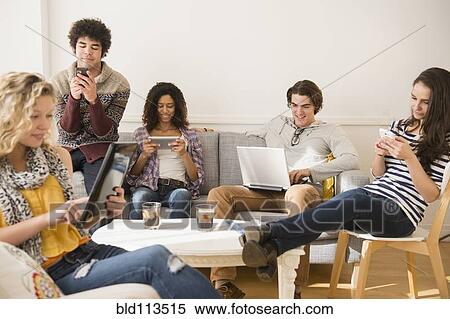 Stock Photography - Friends using technology in living room. Fotosearch