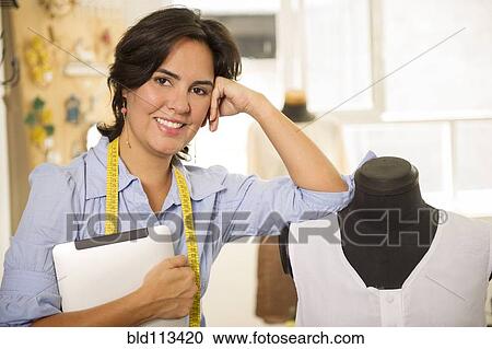Stock Image - Hispanic dressmaker smiling in studio. Fotosearch