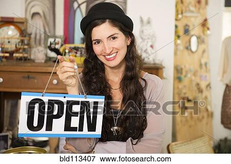 Stock Photo - Hispanic woman holding 'open' sign in shop. Fotosearch
