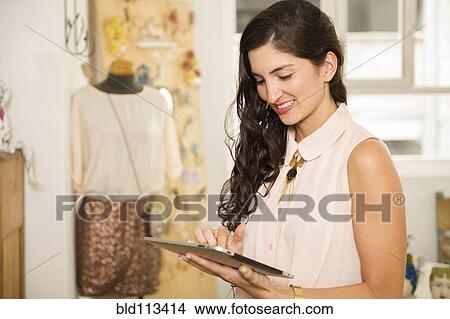 Picture - Hispanic woman using tablet computer in shop. Fotosearch