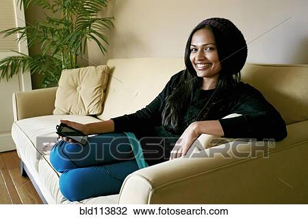 Stock Image - Indian woman using cell phone on sofa. Fotosearch