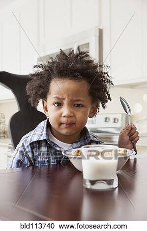 Stock Image - Mixed race boy eating at table. Fotosearch