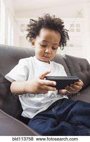 Mixed race boy playing with cell phone on sofa View Large Photo Image Stock Photo - Mixed race boy playing with cell phone on sofa. Fotosearch