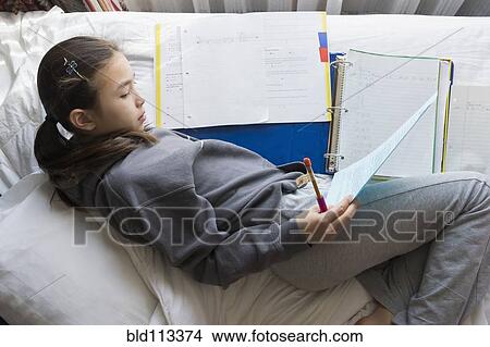 Picture - Mixed race girl doing homework on bed. Fotosearch