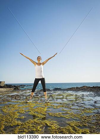 Stock Image - Mixed race runner stretching on rocky beach. Fotosearch
