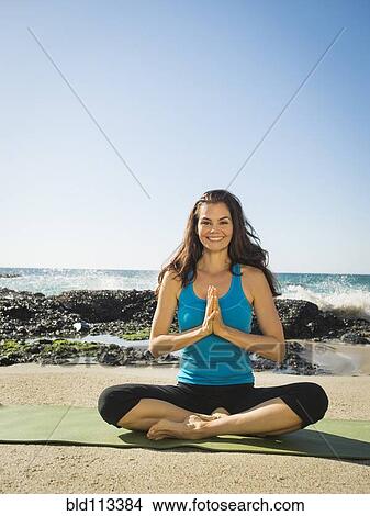 Picture - Mixed race woman meditating on beach. Fotosearch