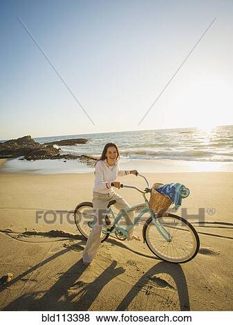 Stock Photo - Mixed race woman riding bicycle on beach. Fotosearch
