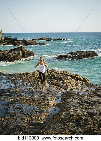 Stock Photo - Mixed race woman running on rocky beach. Fotosearch