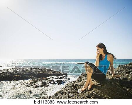 Stock Image - Mixed race woman smiling on rocky beach. Fotosearch