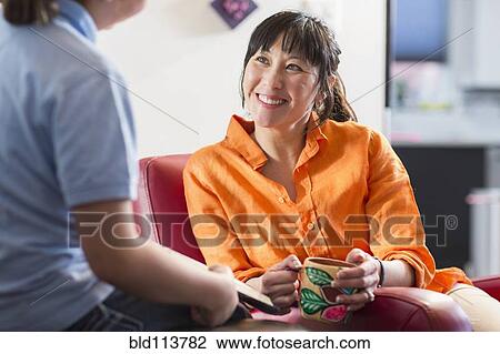 Stock Image - Mother and daughter relaxing in living room. Fotosearch