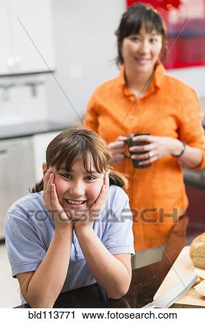 Stock Image - Mother and daughter smiling in kitchen. Fotosearch