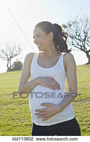 Stock Image - Pregnant mixed race woman holding her belly. Fotosearch