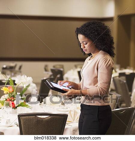 Stock Photo - African American waitress using tablet computer in dining room. Fotosearch