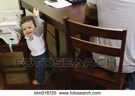 Stock Photography - Baby climbing into high chair at table. Fotosearch