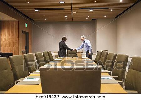 Stock Image - Businessmen shaking hands at meeting table. Fotosearch
