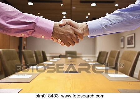 Stock Image - Businessmen shaking hands at meeting table. Fotosearch