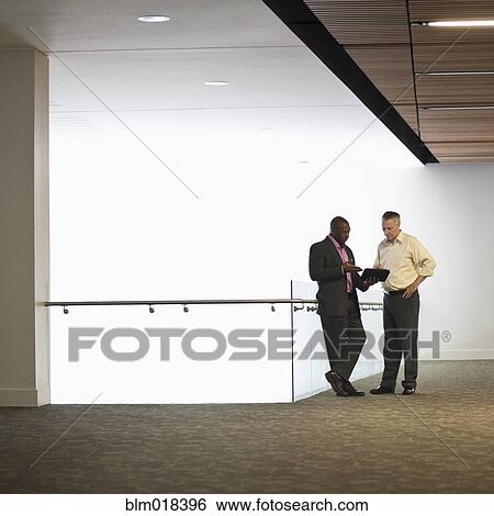 Stock Photograph - Businessmen talking in office hallway. Fotosearch