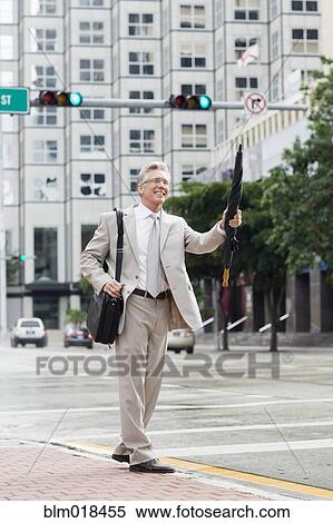 Stock Photography - Caucasian businessman hailing taxi on city street. Fotosearch