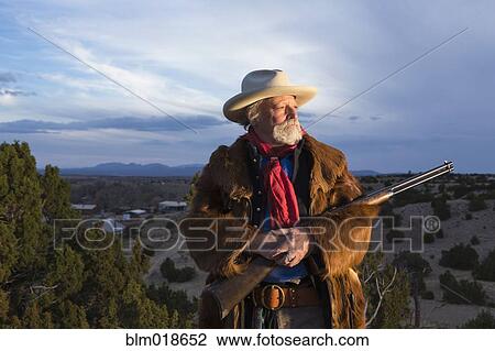 Stock Image - Caucasian man holding gun in dusty landscape. Fotosearch