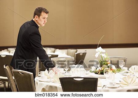 Picture - Caucasian waiter setting tables in dining room. Fotosearch