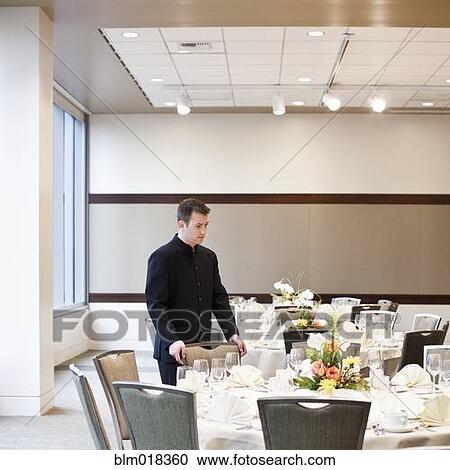 Stock Image - Caucasian waiter setting tables in dining room. Fotosearch