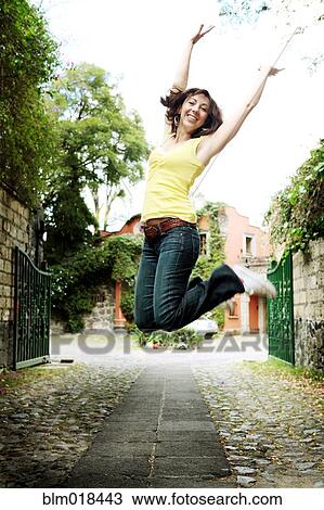 Stock Image - Caucasian woman jumping for joy on city street. Fotosearch