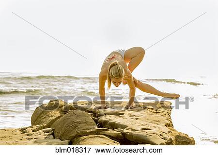 Stock Photo - Caucasian woman practicing yoga on rocky beach. Fotosearch