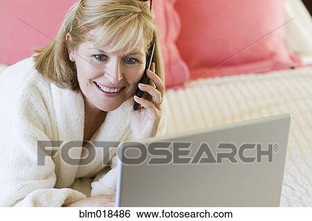 Stock Photograph - Caucasian woman talking on cell phone on bed. Fotosearch