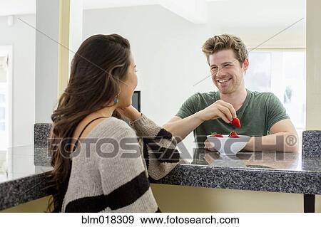 Couple eating fruit together in kitchen View Large Photo Image Stock Photo - Couple eating fruit together in kitchen. Fotosearch