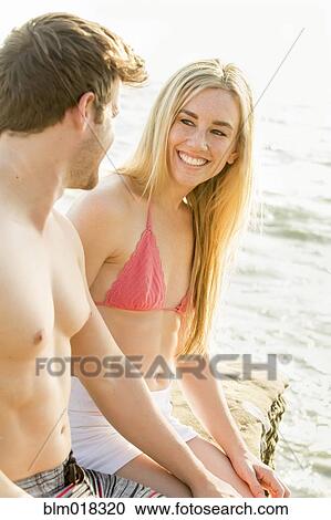 Couple relaxing on rocky beach View Large Photo Image Stock Image - Couple relaxing on rocky beach. Fotosearch