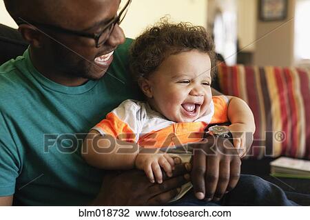 Stock Image - Father and baby laughing on sofa. Fotosearch