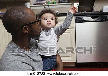 Stock Image - Father holding baby in kitchen. Fotosearch