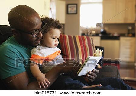 Stock Image - Father reading to baby on sofa. Fotosearch