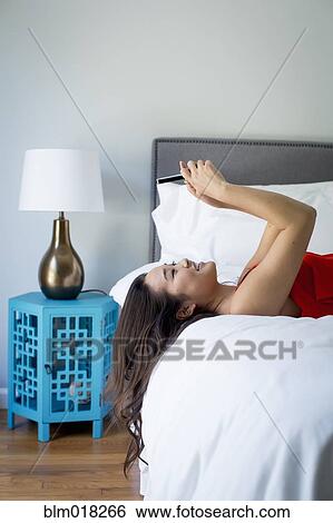Stock Photograph - Japanese woman using cell phone on bed. Fotosearch