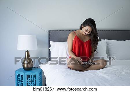 Stock Photo - Japanese woman using tablet computer on bed. Fotosearch