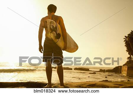 Picture - Man carrying surfboard on beach. Fotosearch