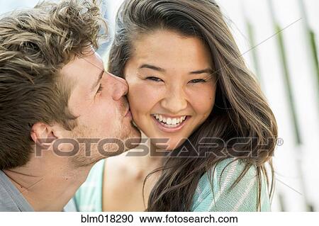 Stock Image - Man kissing girlfriend's cheek outdoors. Fotosearch