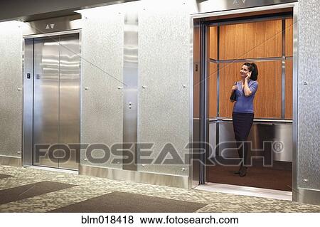 Stock Photo - Mixed race businesswoman on cell phone in elevator. Fotosearch