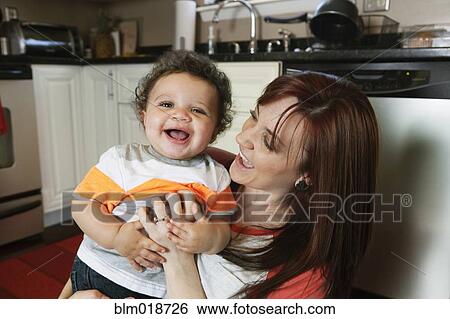 Stock Photograph - Mother and baby playing in kitchen. Fotosearch
