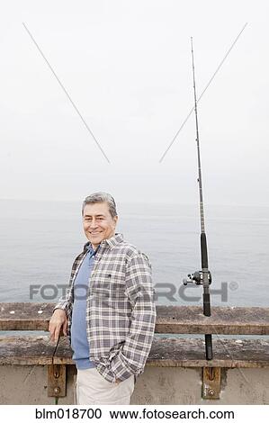 Stock Image - Older Hispanic man fishing on dock. Fotosearch