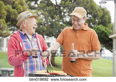 Stock Image - Older men grilling food together outdoors. Fotosearch