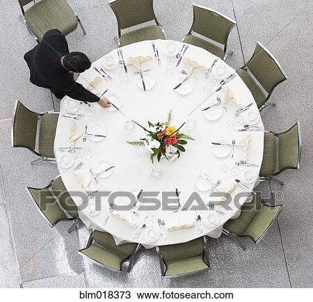 Stock Image - Pacific Islander waiter setting table in dining room. Fotosearch