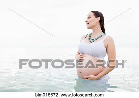 Stock Image - Pregnant Caucasian woman standing in water. Fotosearch