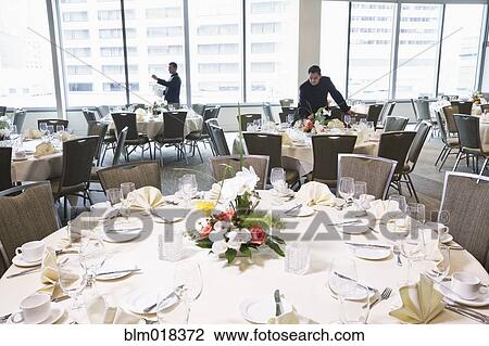 Stock Image - Waiters setting tables in dining room. Fotosearch