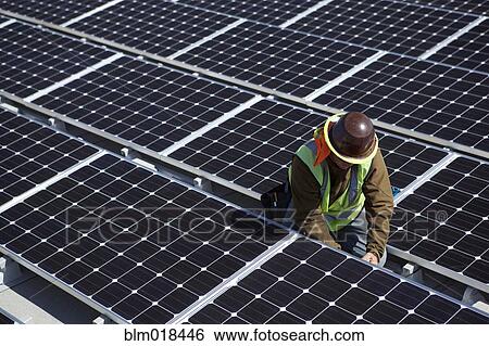 Stock Photograph - Worker examining solar panels outdoors. Fotosearch