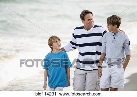 Stock Image - Caucasian father and sons walking on beach. Fotosearch