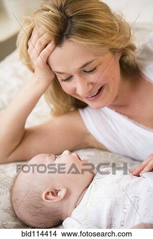 Picture - Caucasian mother and baby laying on bed. Fotosearch